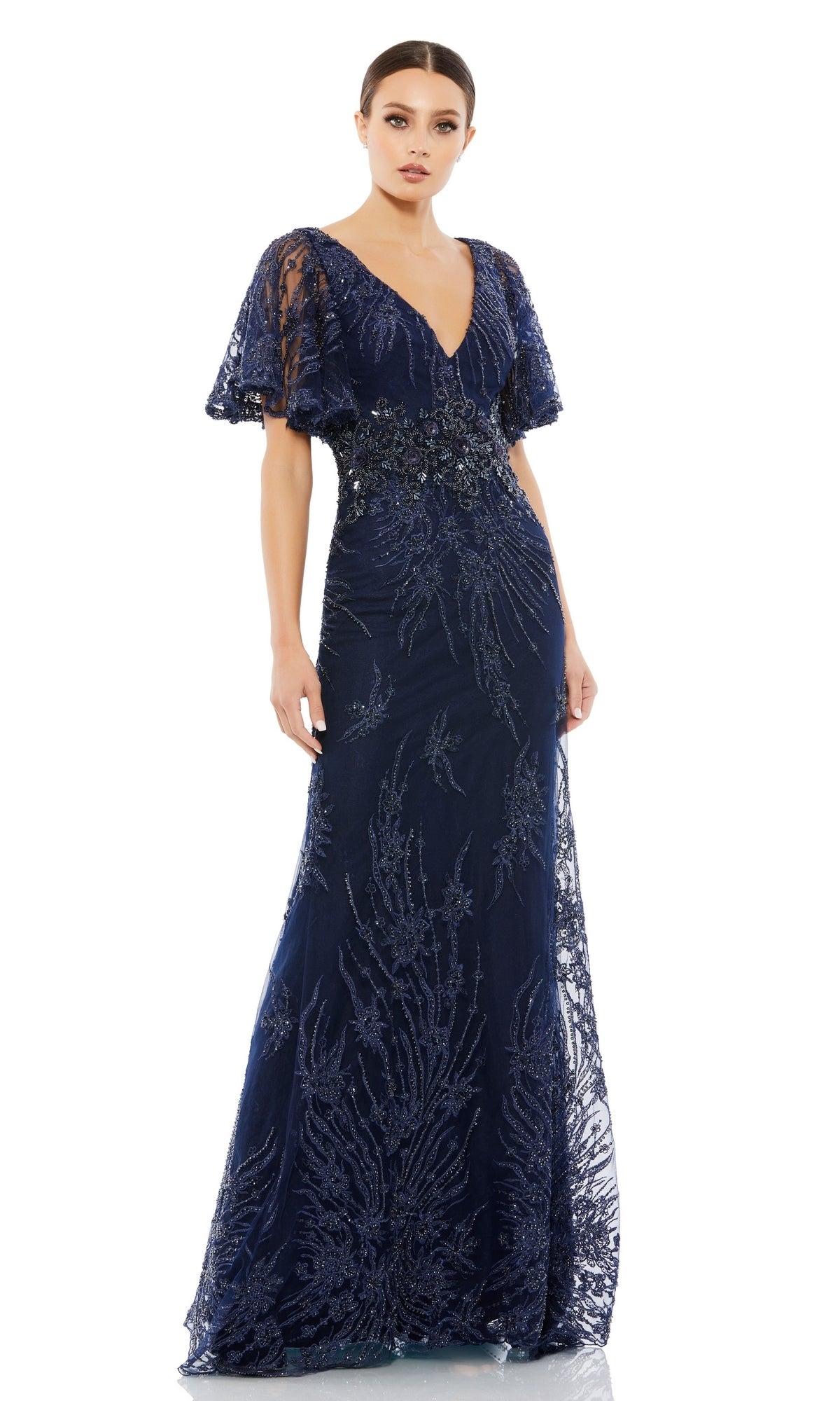 A woman models the Long Formal Dress 67493 by Mac Duggal—a navy blue, floor-length gown with flutter sleeves, intricate beadwork, and a deep V-neckline—standing against a white background.